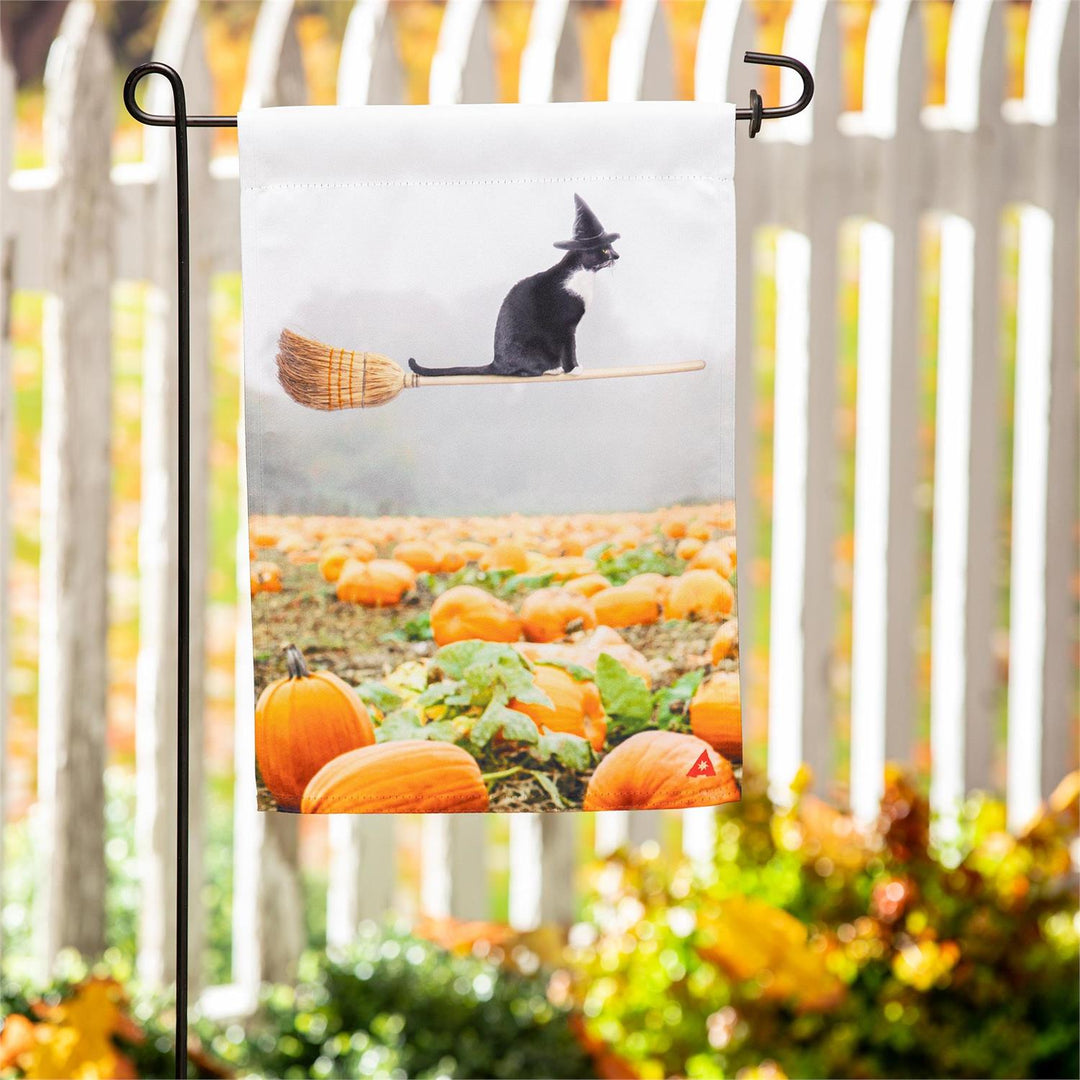 Flying Cat 2 sided Halloween garden flag on a garden stand, showing a black cat in a witch hat riding a broomstick over a pumpkin patch