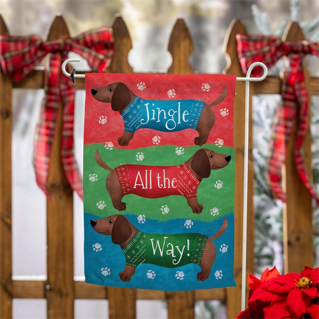 Dachshund Christmas garden flag displayed beside a holiday-decorated wooden fence