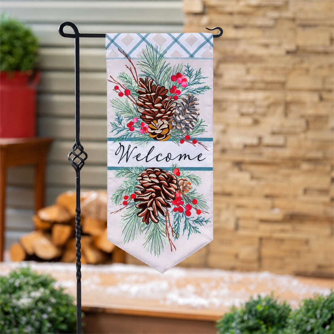 Pinecone Welcome long garden flag displayed on a black stand beside a porch; stand sold separately