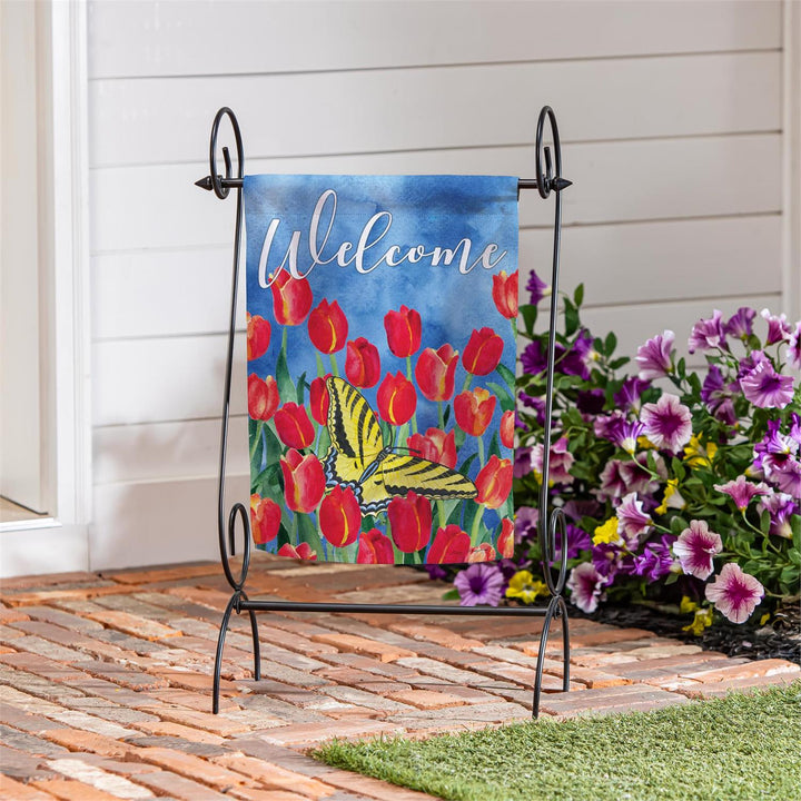 Tulips and butterfly Welcome garden flag hanging on a black garden stand near a porch