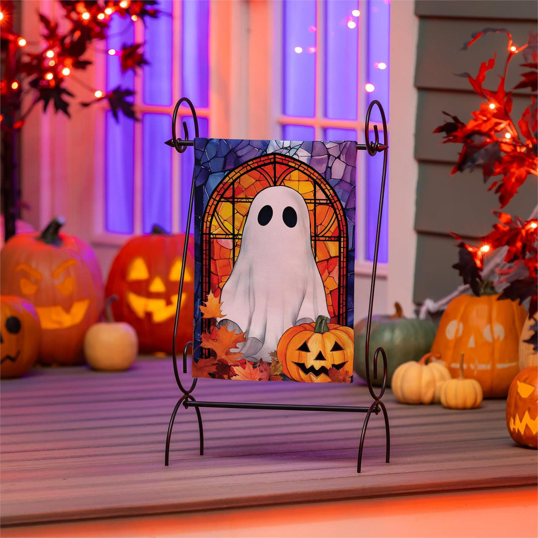 Halloween ghost garden flag displayed on a stand beside pumpkins and fall flowers